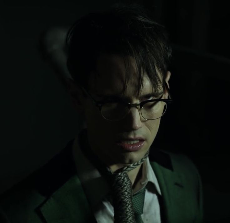 a man wearing glasses and a suit in the dark with a tie around his neck