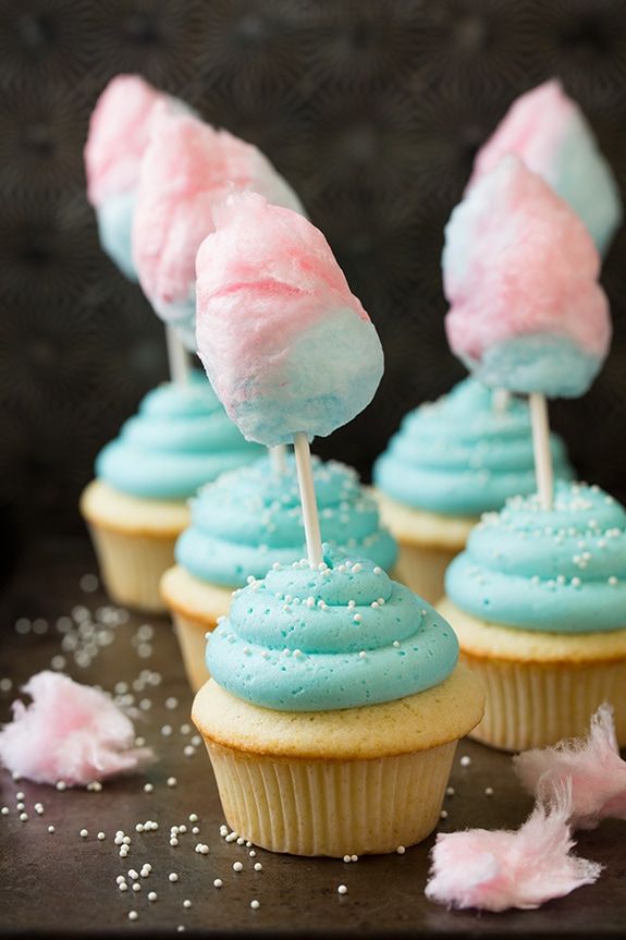 cupcakes with blue frosting and pink marshmallows are on a table