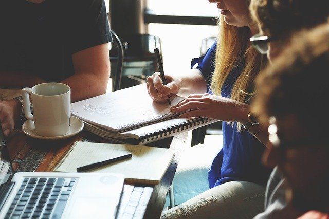 three people sitting at a table with notebooks and coffee