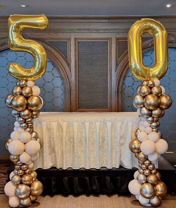 a table topped with balloons in the shape of numbers 50 and fifty surrounded by white and gold balloons