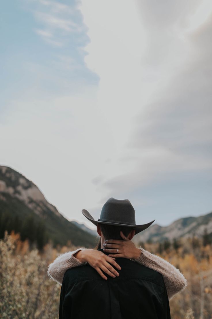 a man wearing a black hat with his back turned to the camera while standing in a field