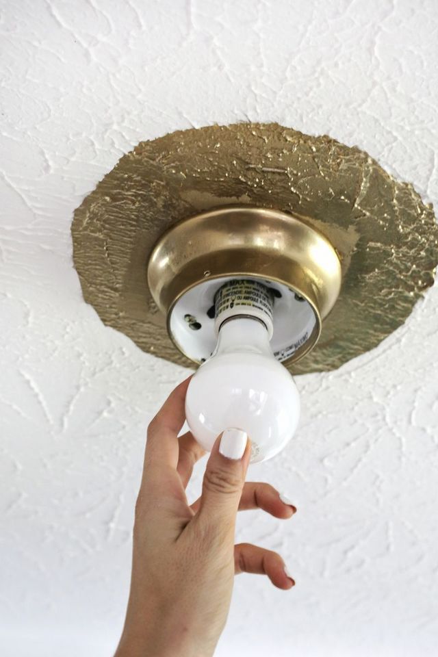 a person's hand is pointing at the light bulb on a ceiling fixture in a white room