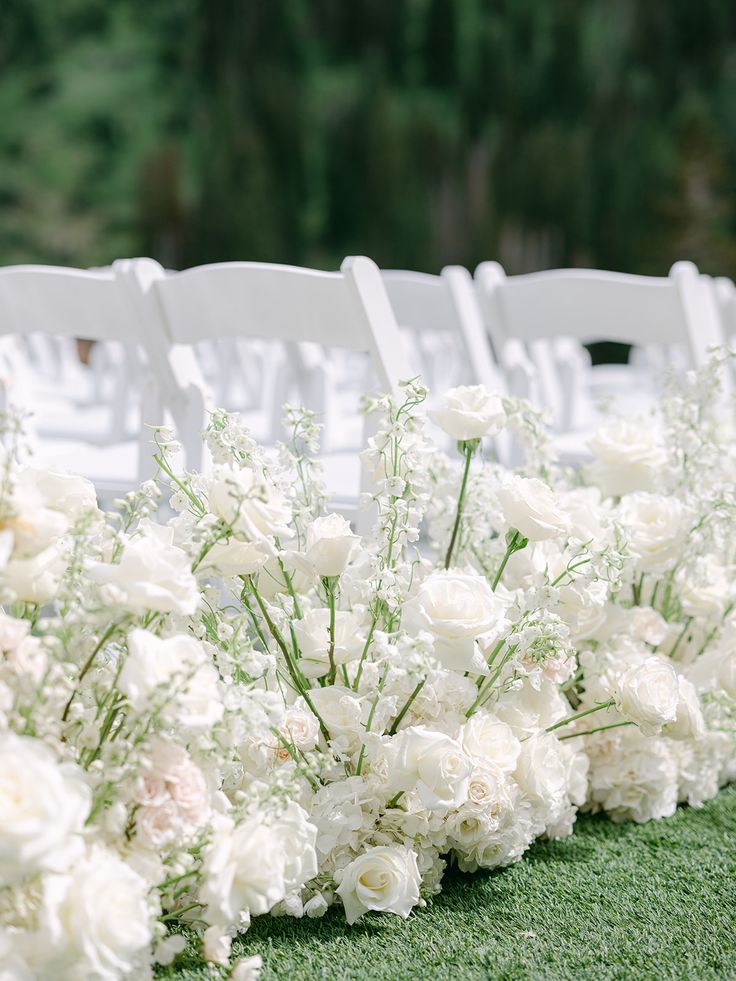 rows of white chairs lined up with flowers on the grass at an outdoor wedding ceremony