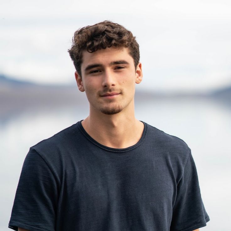 a young man standing in front of a body of water