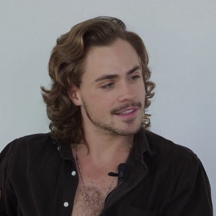 a man with long hair and no shirt on sitting in front of a white wall