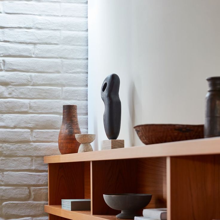 some vases and bowls are sitting on a shelf in front of a brick wall