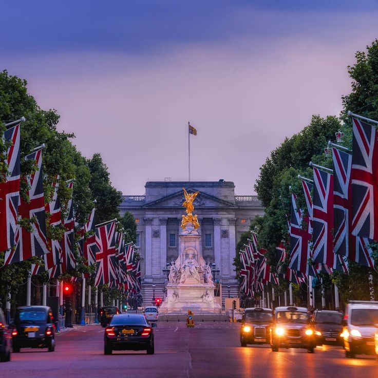 cars driving down the road in front of a building with flags flying from it's sides