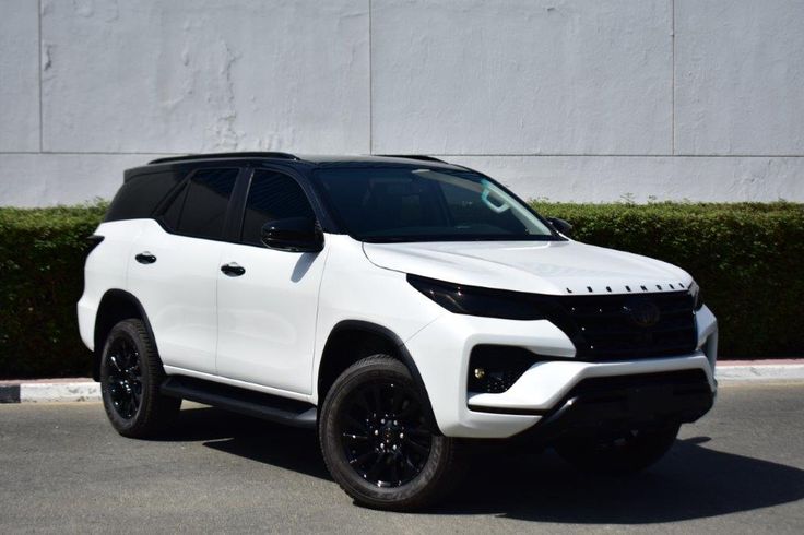 a white suv is parked in front of a building with hedges and bushes behind it