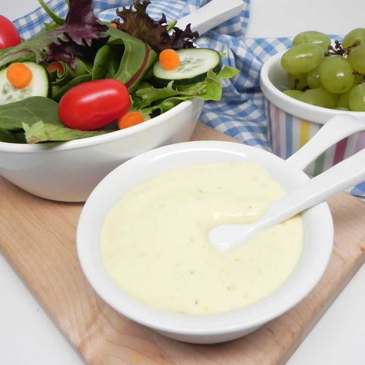 two bowls filled with salad sitting on top of a wooden cutting board next to grapes