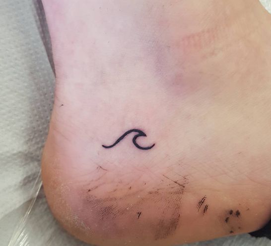 a small wave tattoo on the foot of a woman's left foot, with black ink