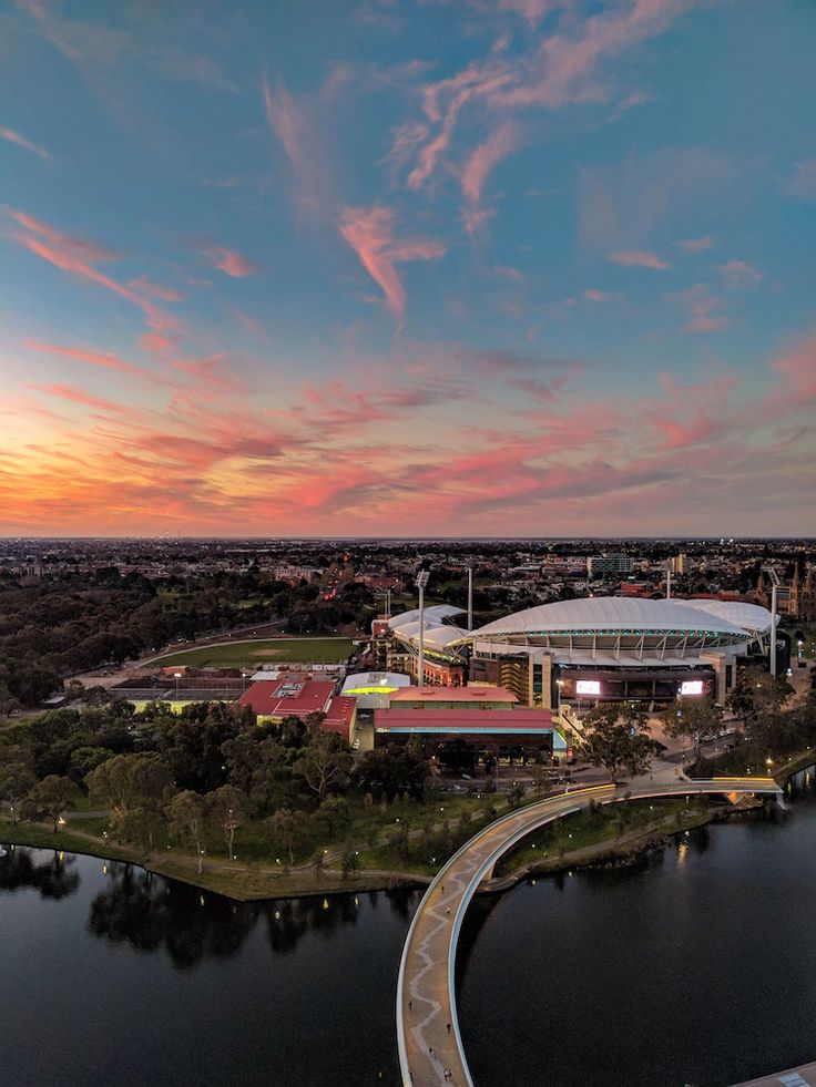 an aerial view of the sun setting over a stadium and river with buildings in the background