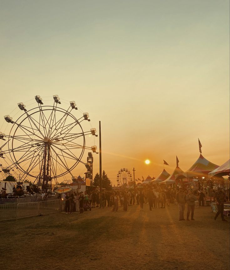 the sun is setting over an amusement park with ferris wheel and tents in the background