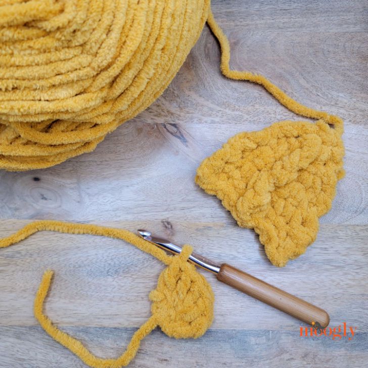 two crocheted pieces of yellow yarn next to a knitting needle on a wooden surface