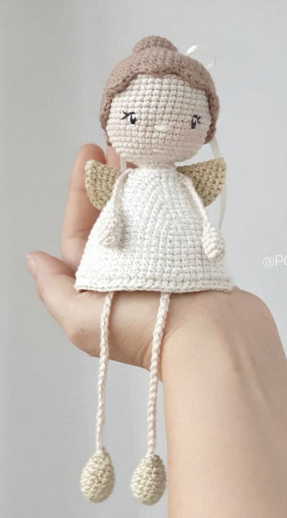 a small crocheted angel doll is held in someone's hand, wearing a white dress