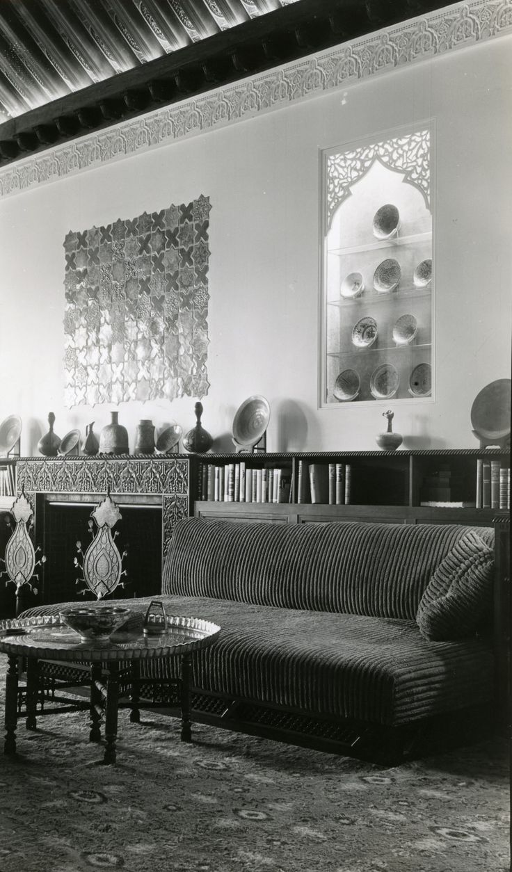 an old photo of a living room with couches, tables and bookshelves