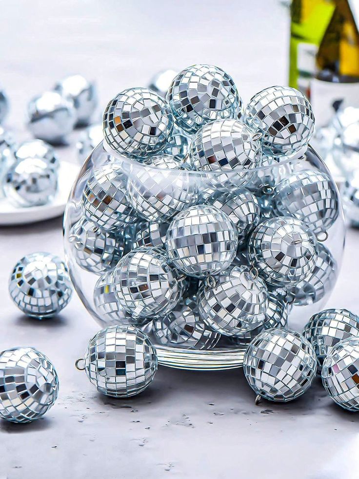 a bowl filled with silver disco balls on top of a table next to wine bottles