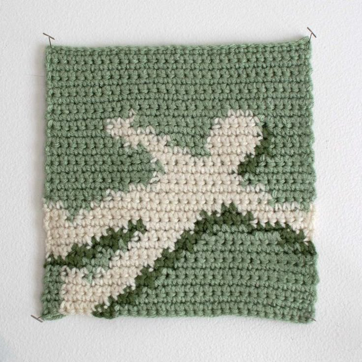 a green and white crocheted square with an airplane on it