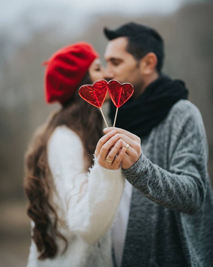 a man and woman holding two red heart shaped lollipops in their hands