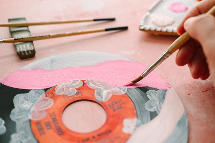 someone is painting an old record with pink and white paint on the table next to some brushes