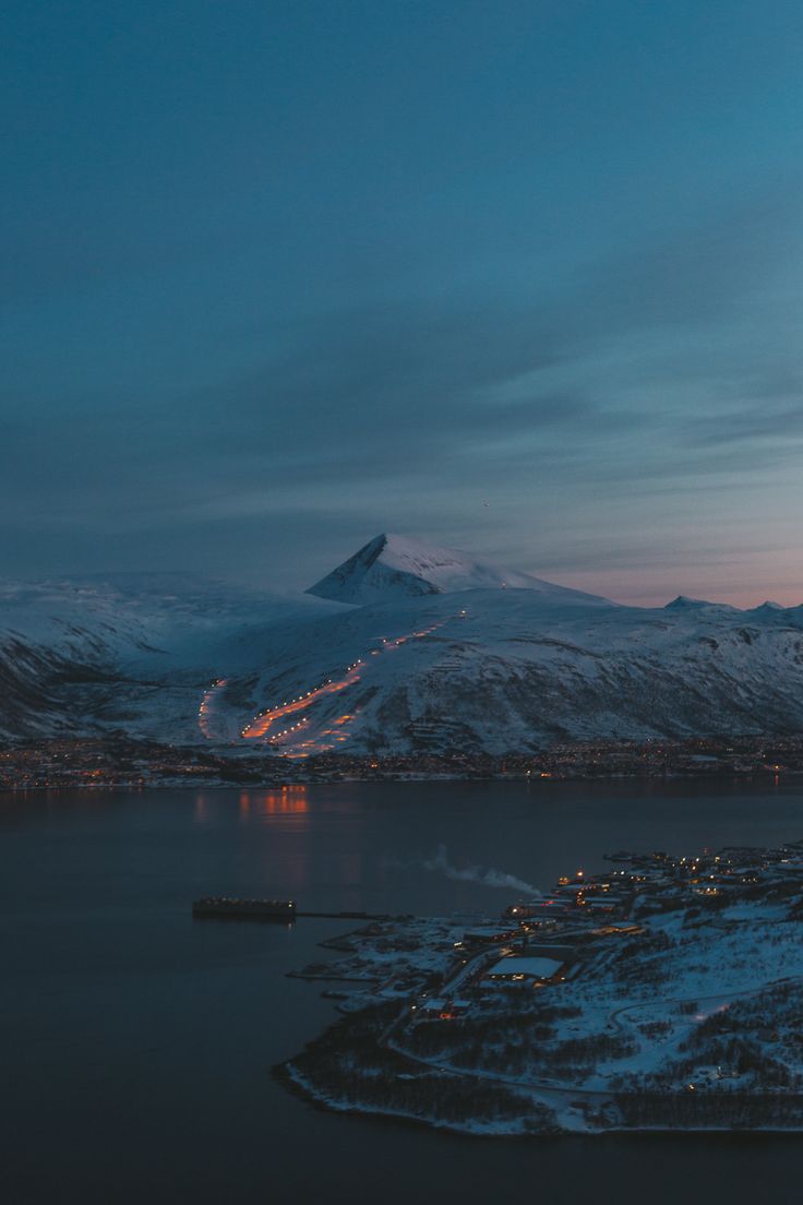 an aerial view of a city and mountains at night with snow on the ground, lights in the distance