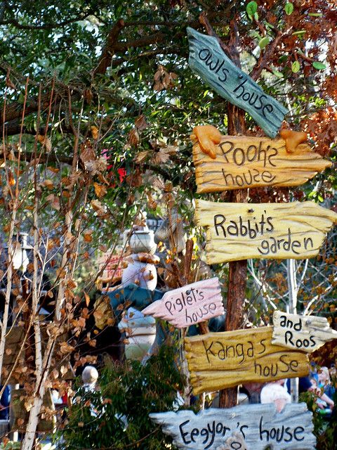 several wooden signs hanging from the side of a tree in front of some bushes and trees