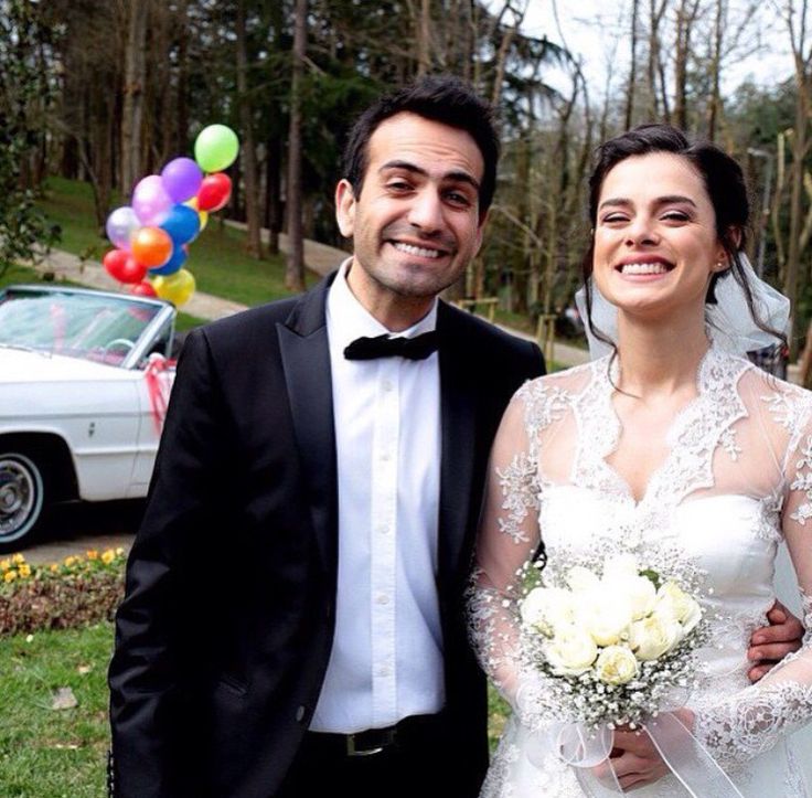 a bride and groom posing for a photo in front of their wedding car with balloons