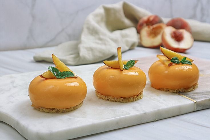 four small desserts are arranged on a marble tray with peaches in the background