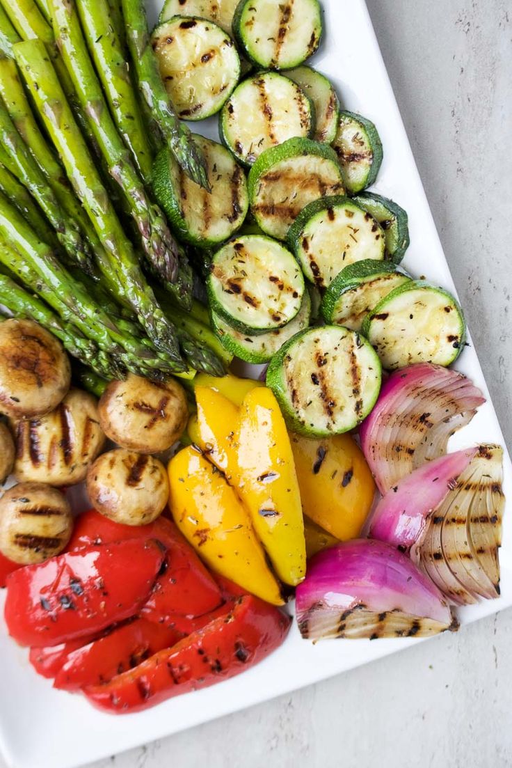 grilled vegetables are arranged on a plate with asparagus, red peppers and green onions