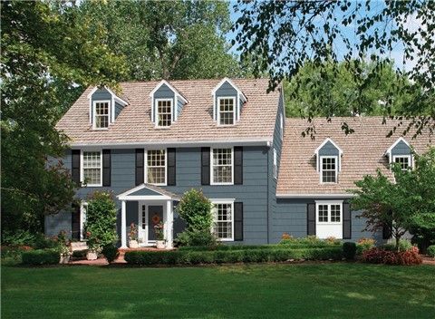 a large blue house with white trim and windows on the front, surrounded by lush green trees