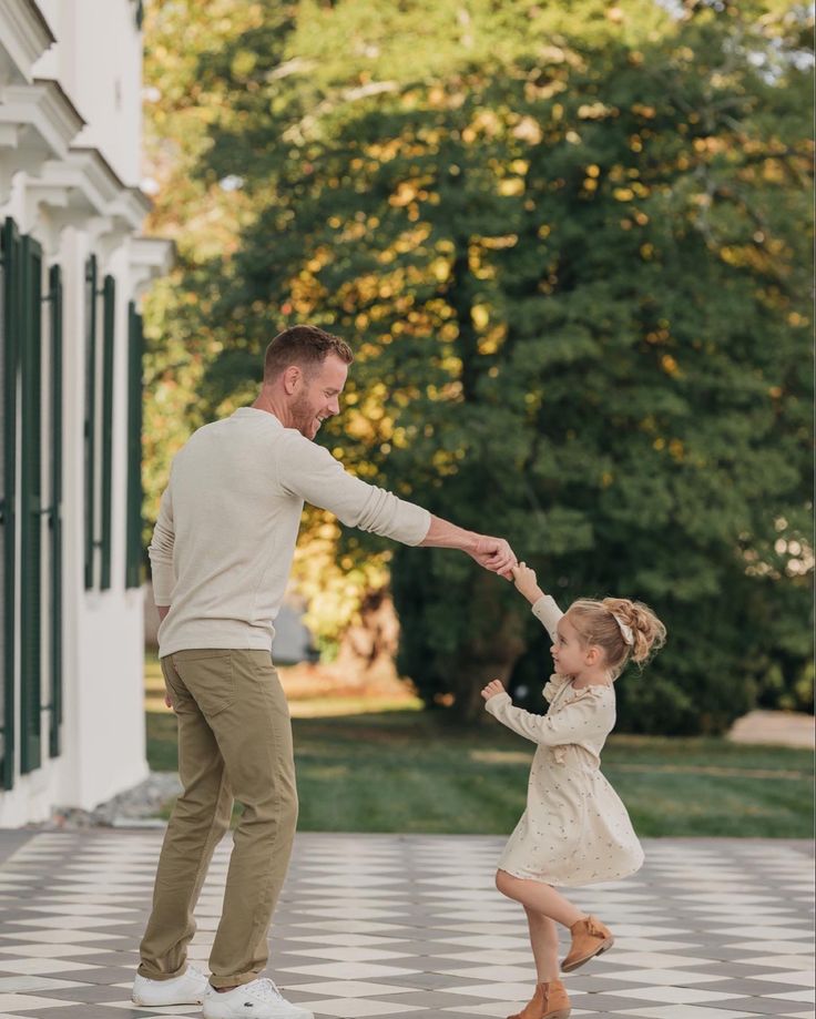 a father and daughter playing with each other in front of a house on a checkered floor