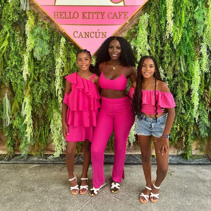 three women standing in front of a sign that says hello kitty cafe cancun