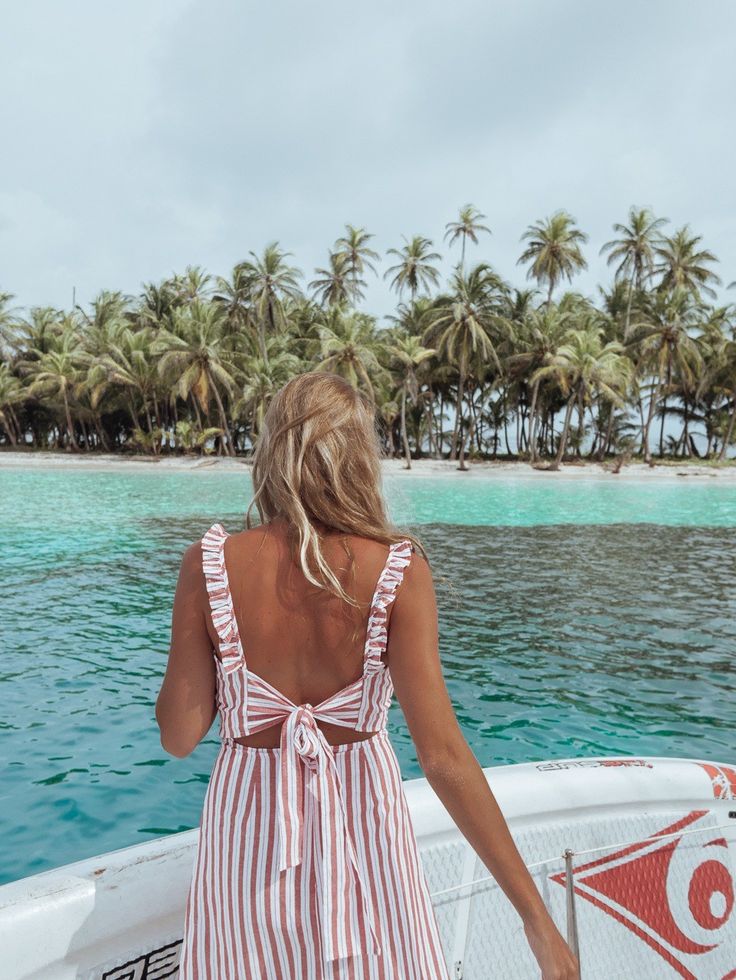 a woman in a red and white striped dress standing on a boat looking out at the ocean