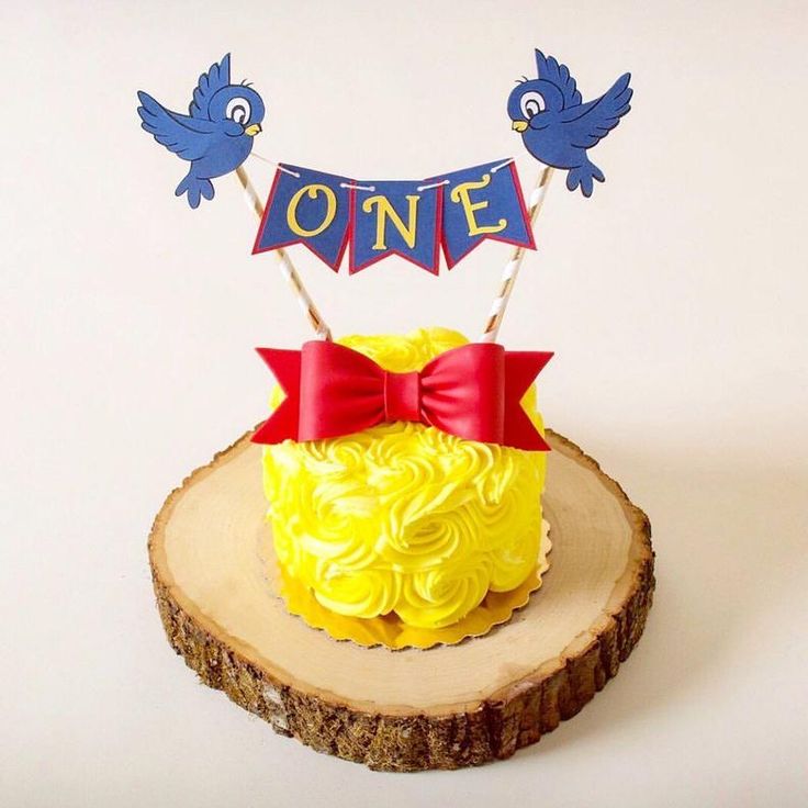 a cake with yellow frosting and red bow on top sitting on a piece of wood