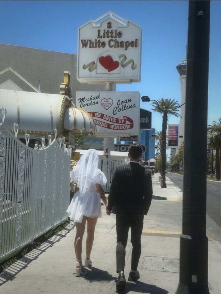 a man and woman are walking down the sidewalk in front of a white chapel sign