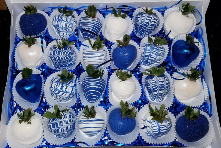 a box filled with blue and white chocolate covered strawberries on top of each other