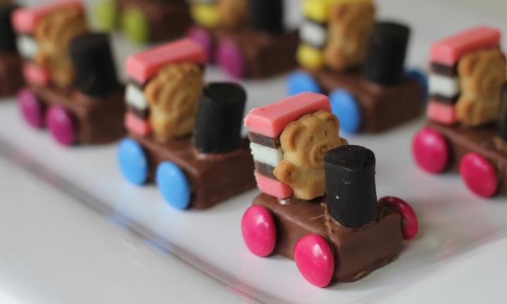 small toy train made out of chocolate and candy on a white tray with pink, blue, yellow, and green candies