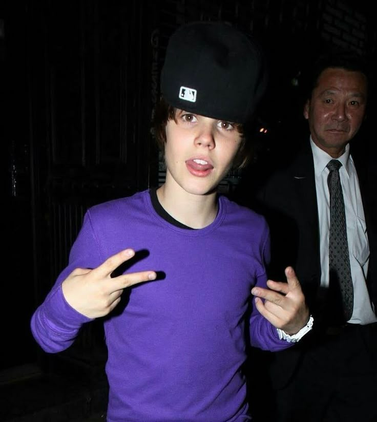 a man in a purple shirt and black hat with his hands out to the side