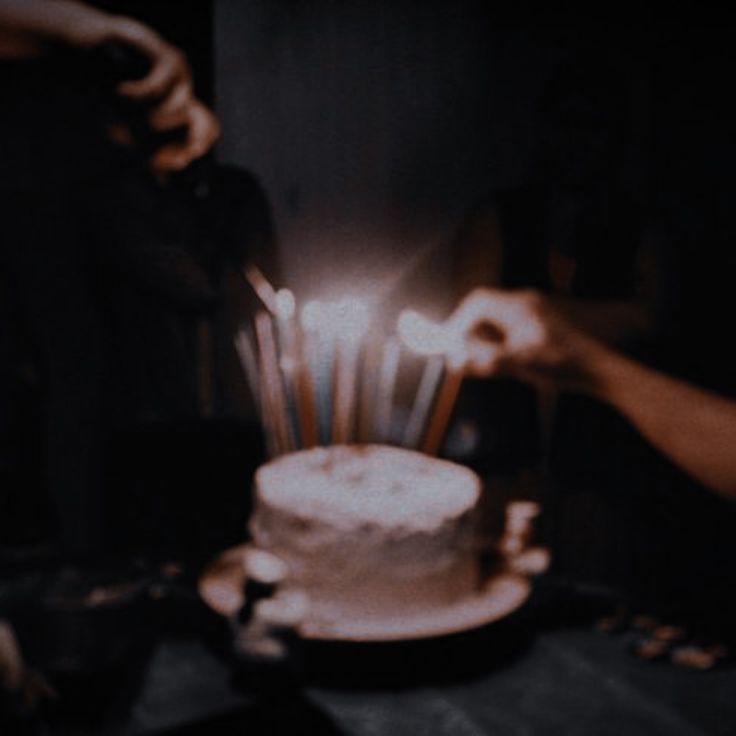 someone lighting candles on top of a cake with white frosting and icing, in the dark