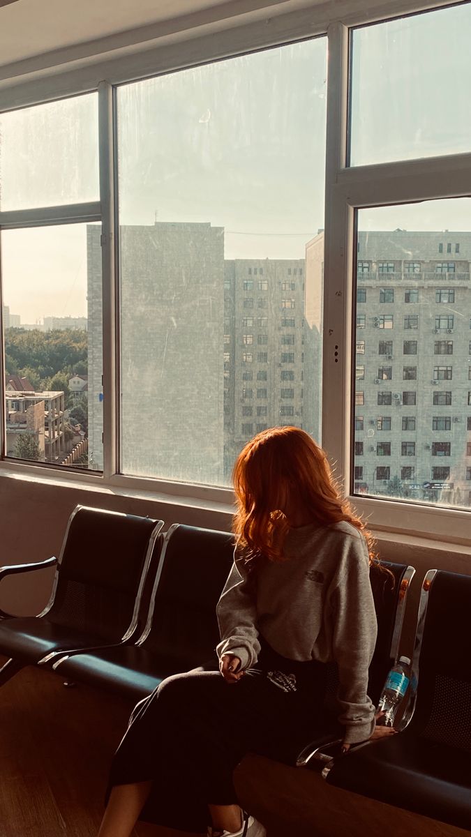 a woman sitting on a bench in front of a window looking out at the city