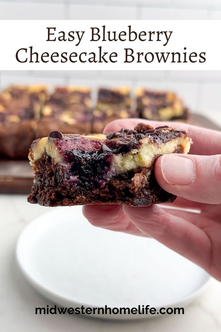 a hand holding a piece of blueberry cheesecake brownies