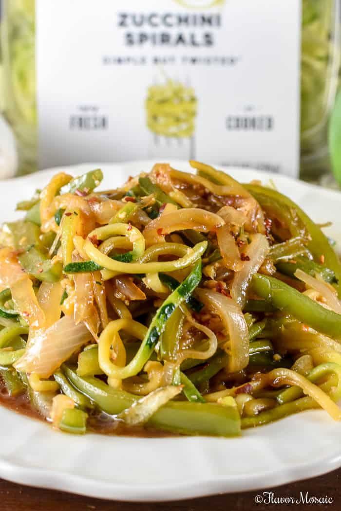 a white plate filled with noodles and vegetables on top of a wooden table next to a bottle