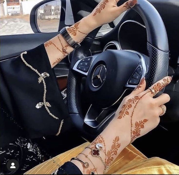 a woman with henna on her arm driving a car and holding the steering wheel