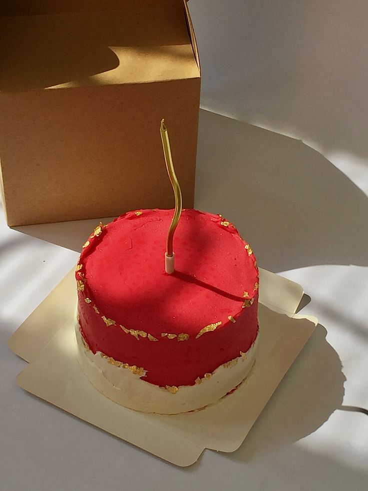 a red and white cake sitting on top of a table next to a brown box