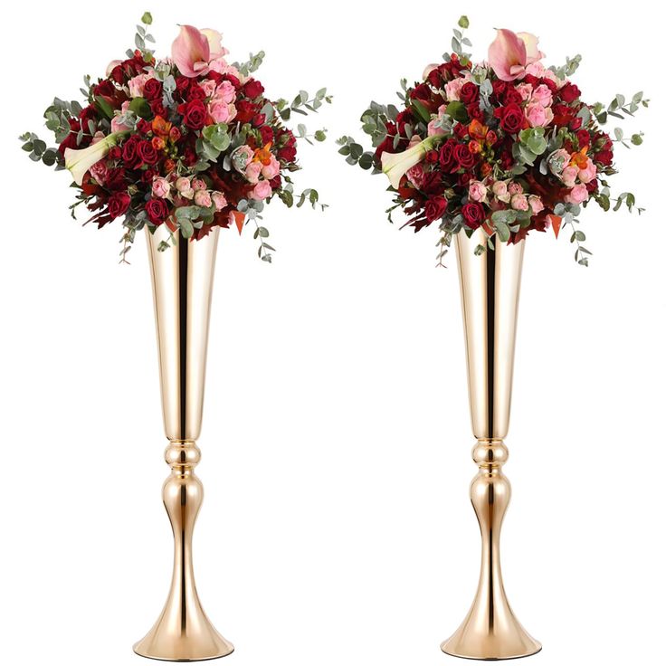 two tall gold vases with red and pink flowers in them, one is filled with greenery