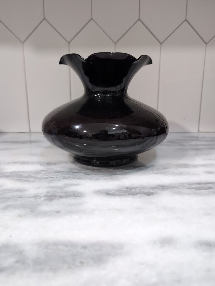 a black vase sitting on top of a marble countertop next to a white tiled wall