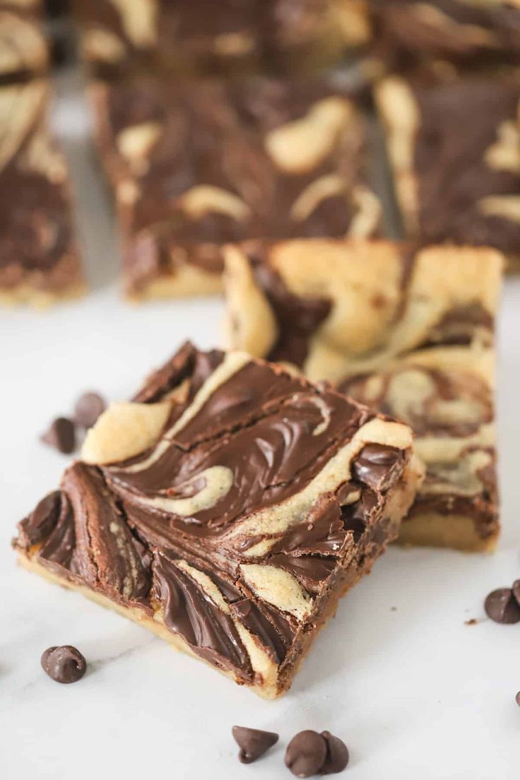 chocolate and peanut butter swirl bars cut into squares on a white surface with chocolate chips scattered around them