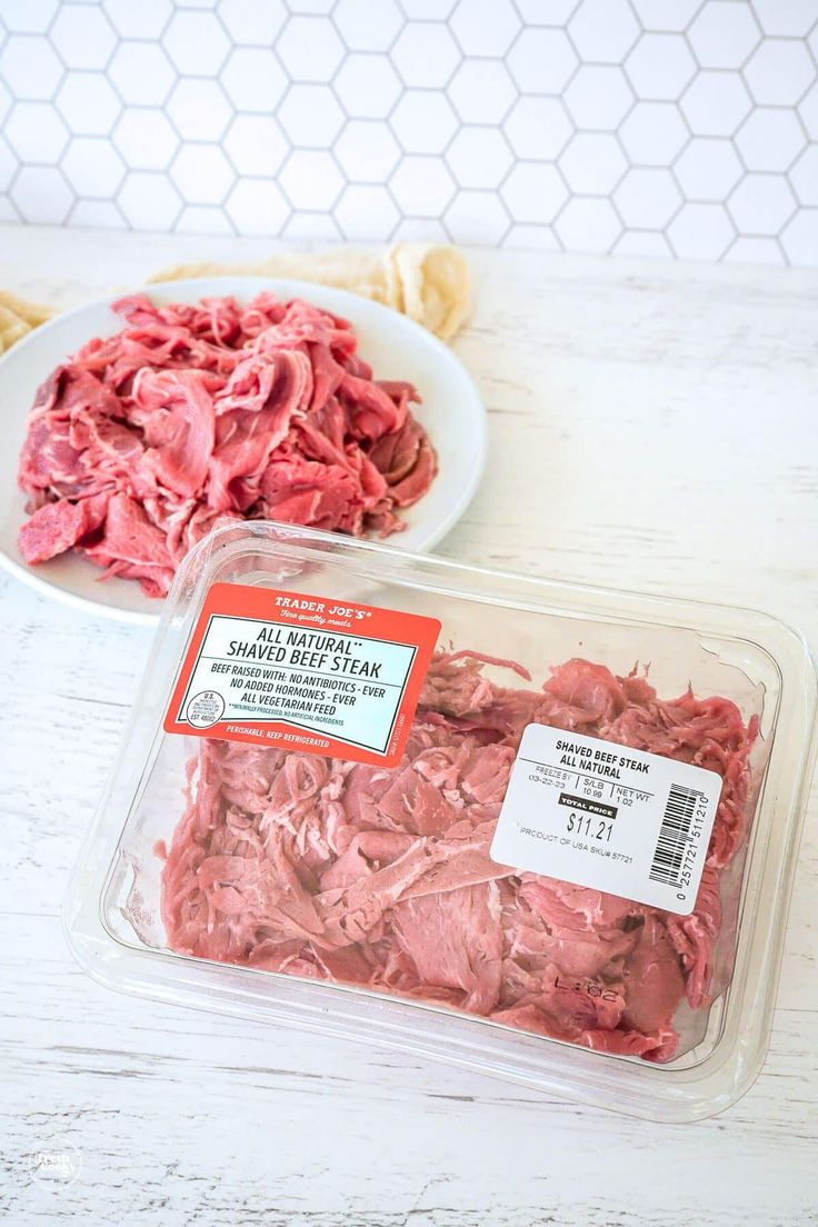 two plastic containers filled with meat sitting on top of a white wooden table next to a plate of corned beef