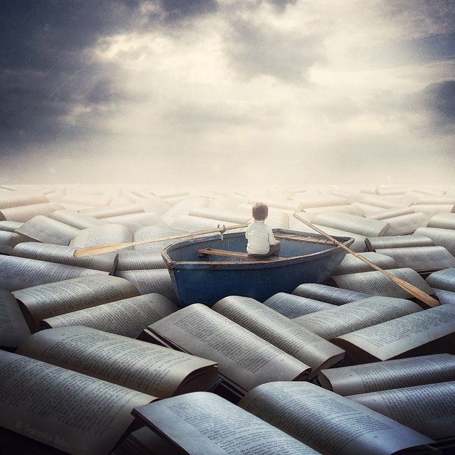 a man sitting in a row boat surrounded by large book pages on the ground and cloudy sky