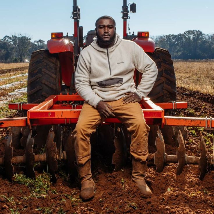 a man sitting on top of a red tractor in the middle of a dirt field