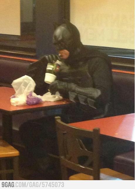 a person in a batman costume sitting at a table drinking from a cup with the caption, i'll have a 7